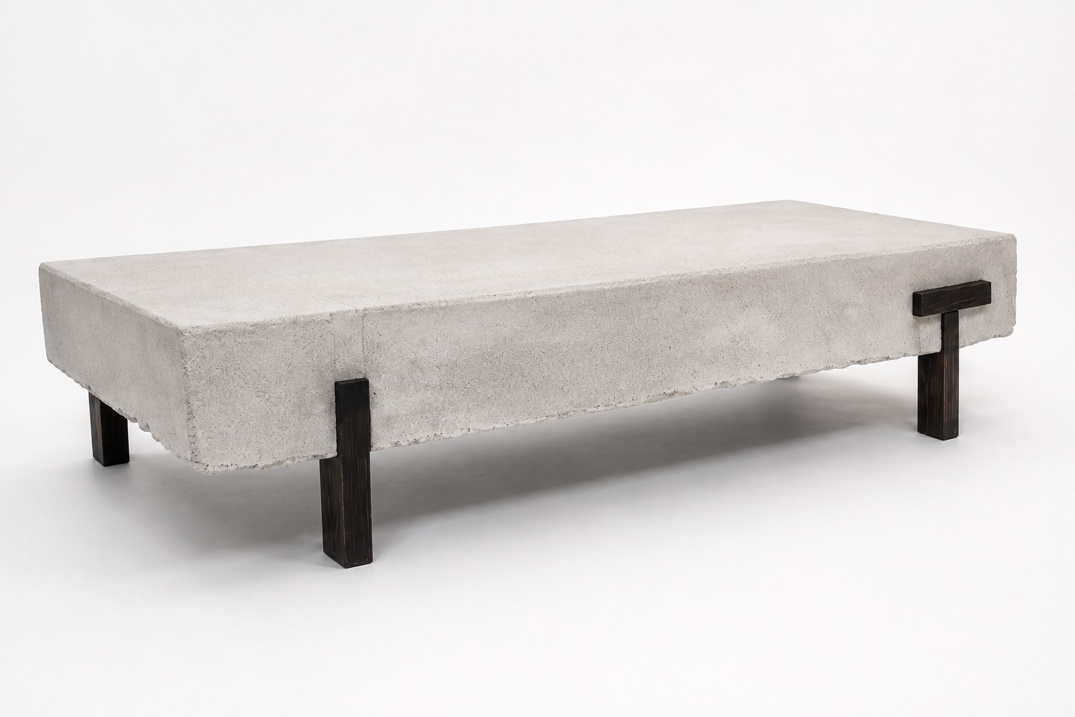 PIEZA 001, a low coffee table with a thick mineral-finish top and dark T-shaped wooden legs, photographed at a three-quarter angle in the studio.