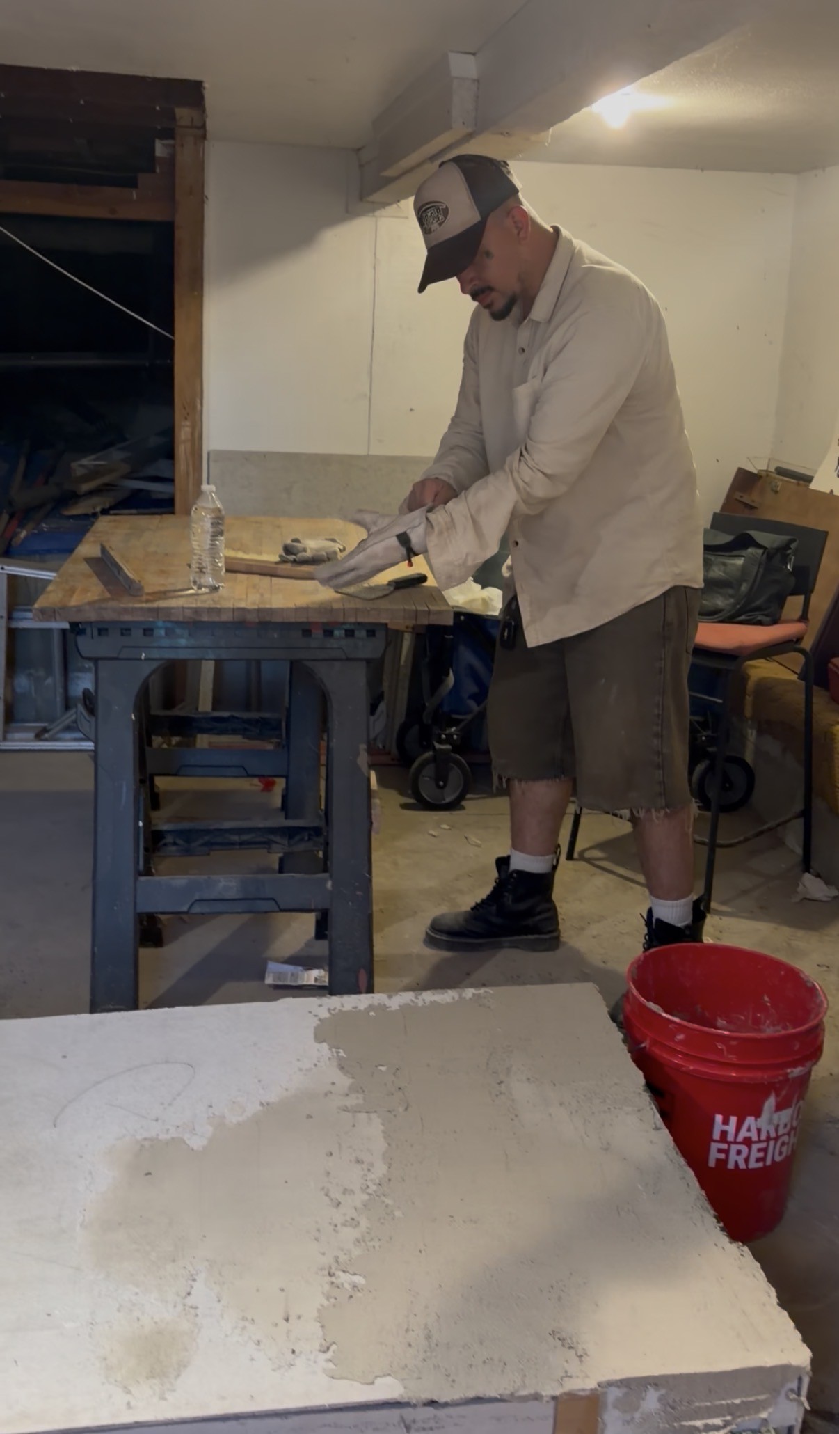 The artist standing at a workbench in the workshop, working a hand tool over the surface of PIEZA 001 mid-construction.